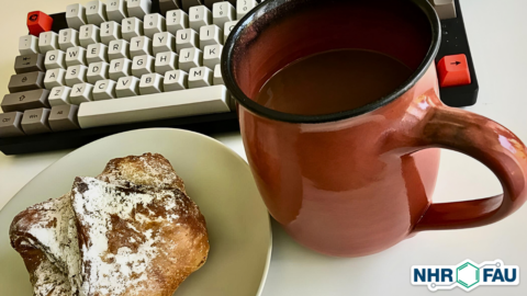 A piece of sweet pastry on a plate and a cup of coffee placed in front of a retro style keyboard.