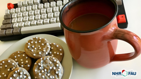 A cup of coffee and a plate withchristmas cookies on it in front of a computer keyboard.