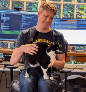 A picture of developer Matt Godbold sitting in his office with a black and white cat on his lap.