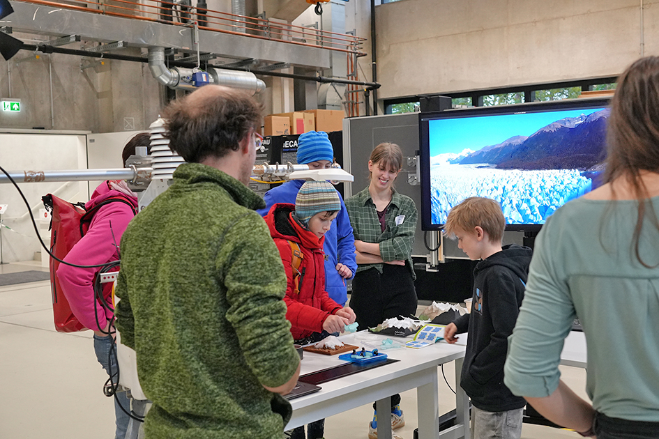 This image captures a group of people, engaged in an educational activity. The background features various pieces of technical equipment, suggesting a research or engineering environment. The overall atmosphere appears to be one of engaged learning and curiosity.