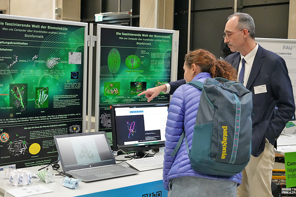 This image captures two adults engaged in a discussion about a scientific topic at a university event. The posters feature text and diagrams. The title on the poster reads: 