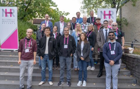 A group of people from NHR@FAU, wearing pink badges from the NHR Conference 2025, standing in front of a building of the University of Göttingen.