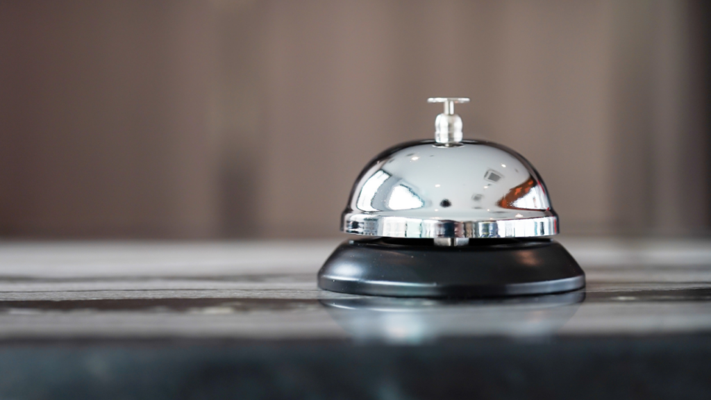 A silver bell on a wooden board, probably at a reception desk.