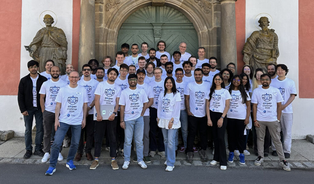The image depicts a large group of people posing together in front of a historic building. The individuals are predominantly wearing white T-shirts printed with "dAIper Challenge 2026," suggesting a competition in the field of artificial intelligence.