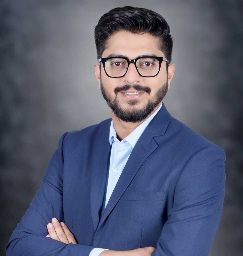 A picture of one of the colleagues at NHR@FAU: a man with dark hair and a dark beard wearing glasses and a blue suit.