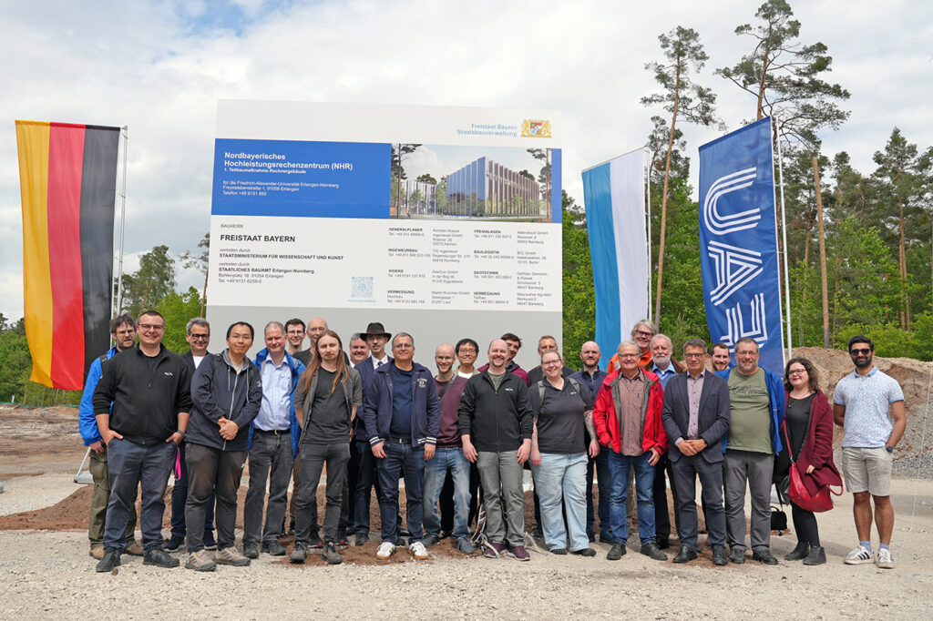 The image shows the NHR@FAU Board gathered at a construction-site ceremony for a research computing facility. The sign behind the group announces the construction of the Nordbayerisches Hochleistungsrechenzentrum (NHR) and includes a rendering of the future building.
